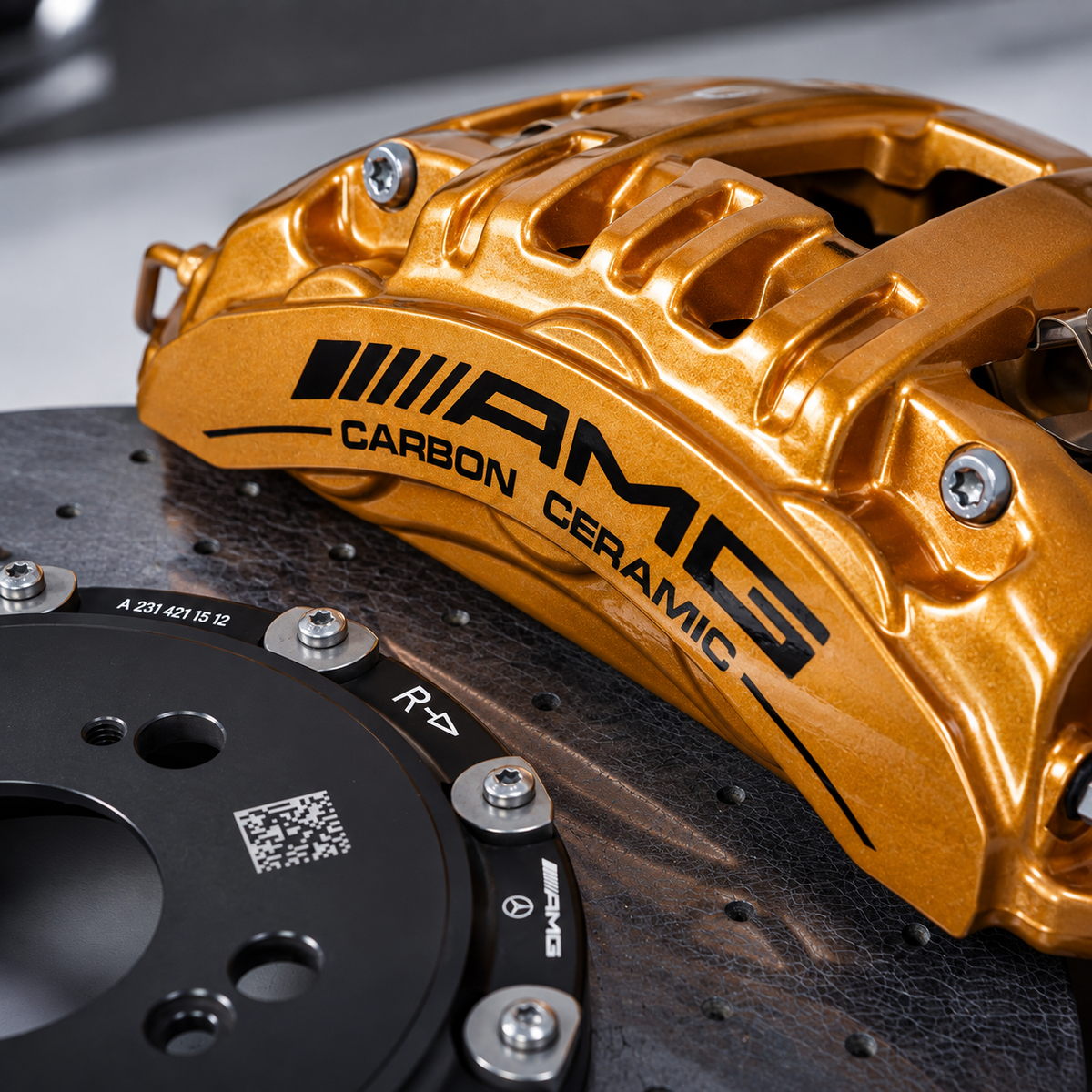 Close-up of a metallic gold AMG brake caliper with black 'AMG CARBON CERAMIC' lettering, mounted over a black ventilated brake rotor.
